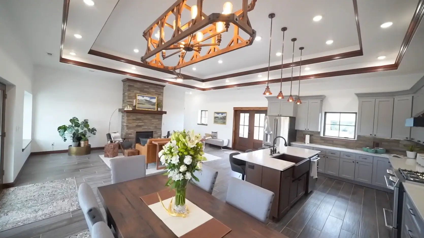 Interior photo of a home built by Harvell Homes in Powell, Wyoming featuring a luxurious and furnished open-floor kitchen, dining, and living room with tray ceiling and wood-look plank tile flooring